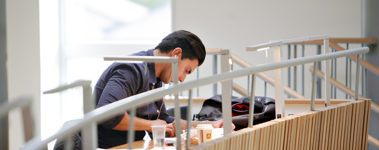 Manlig student som sitter fokuserad och böjd över sitt studiematerial i biblioteket